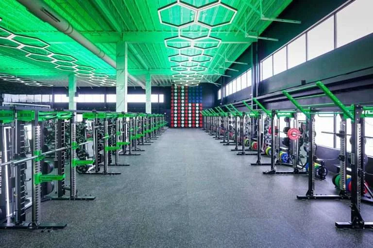 Aisle between rows of power racks under green hexagon lights at Fusion Gyms Warminster